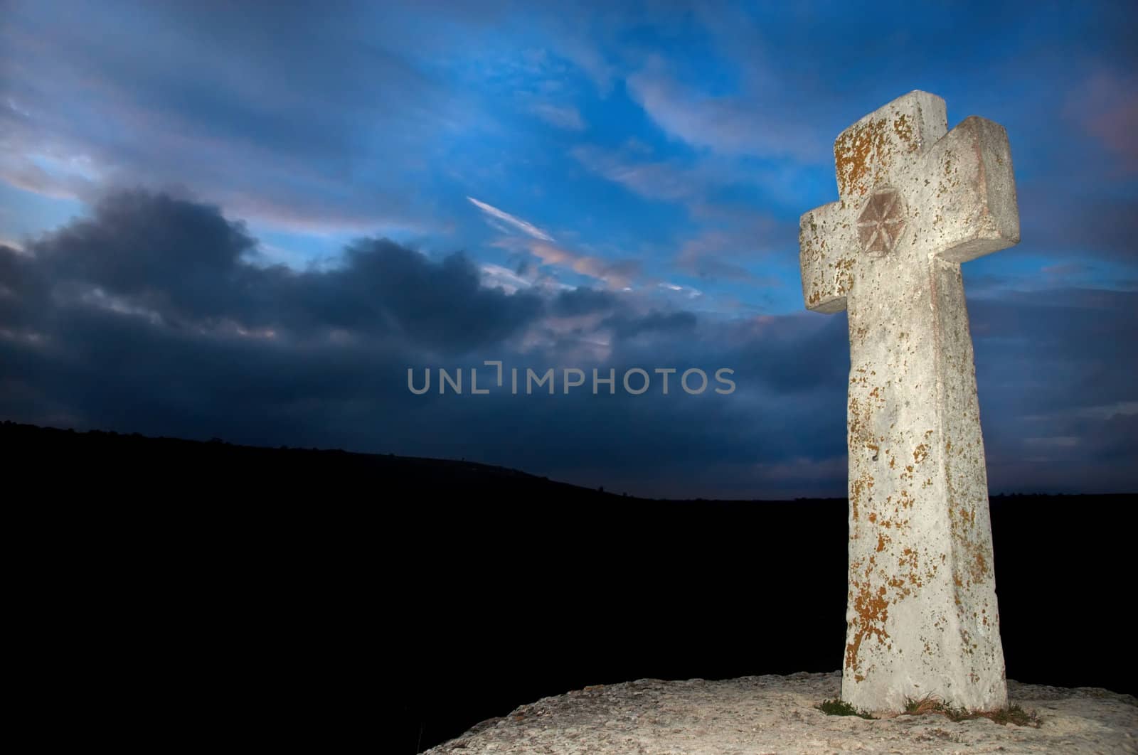 brightly lit stone cross on dark sky background