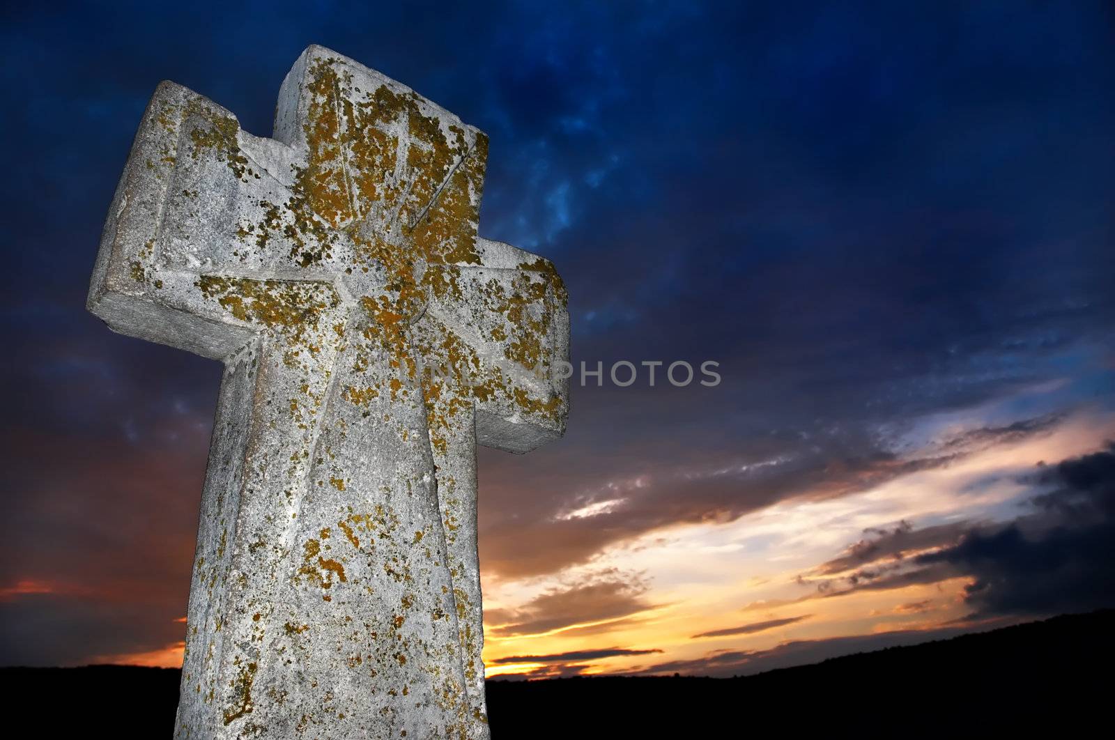 brightly lit stone cross on the sunset background