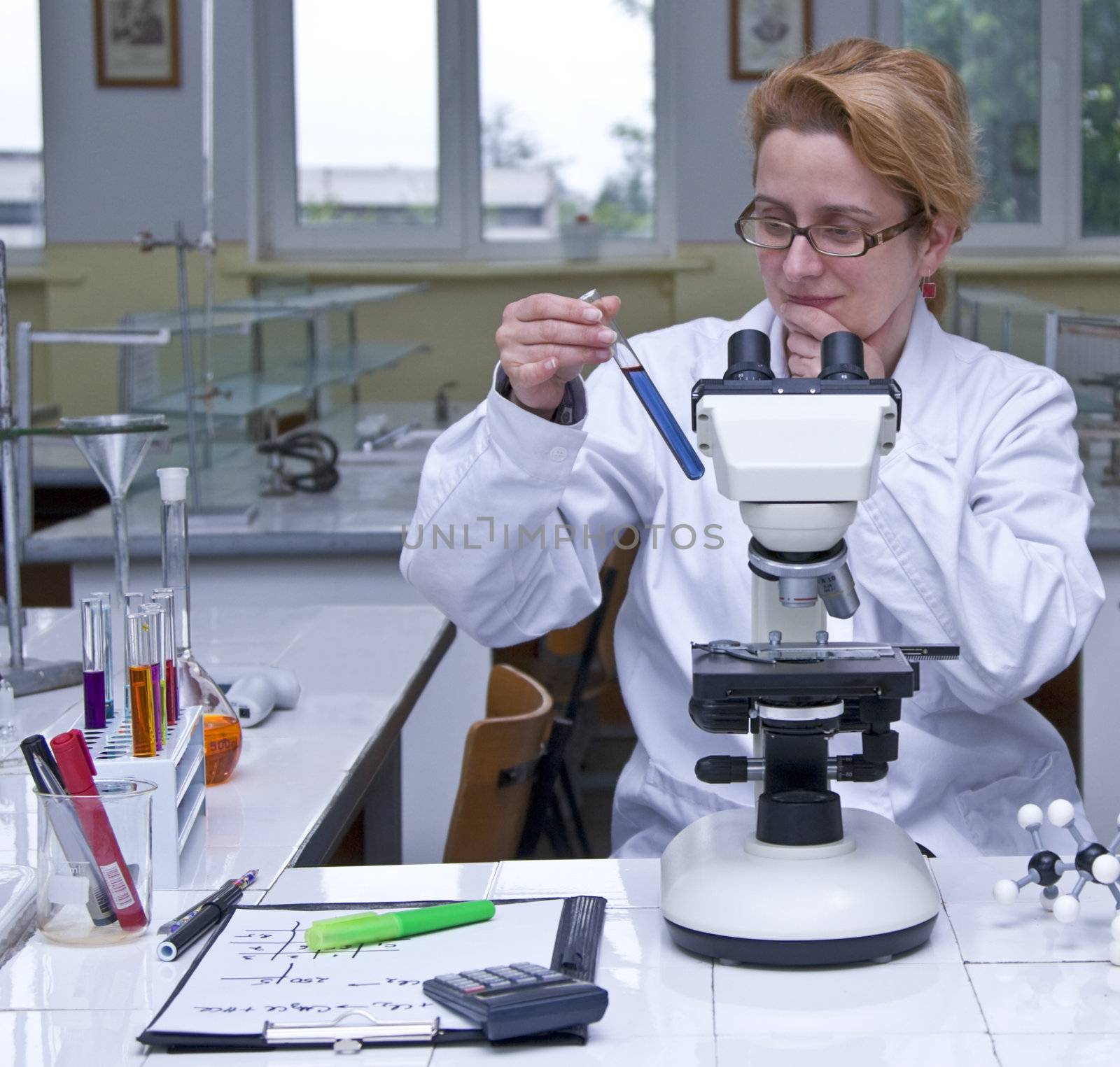 Female researcher looking at a test tube containing a solution, at her workplace in a laboratory.All the inscriptions are mine. 