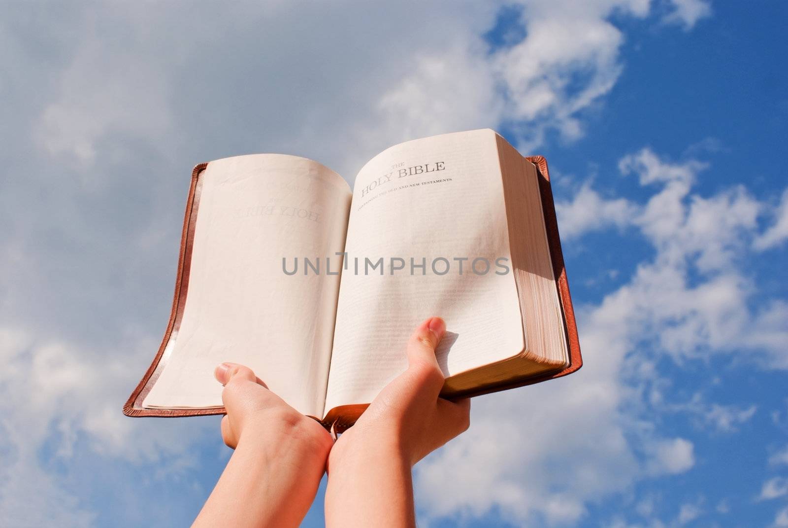 Hands hold the open Bible against blue sky by AndreyKr
