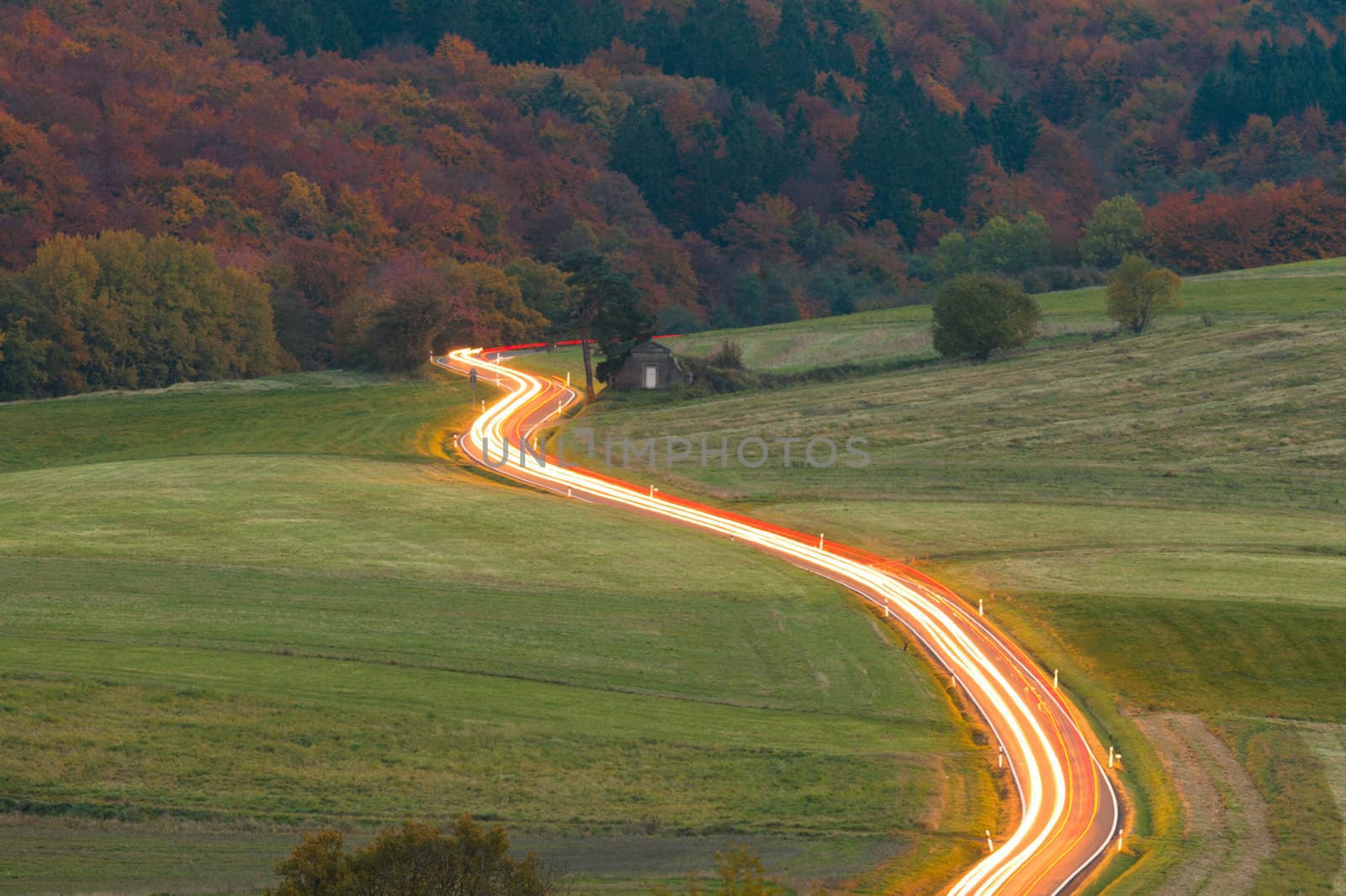 Light trails of moving vehicles on rural country road at night fall.