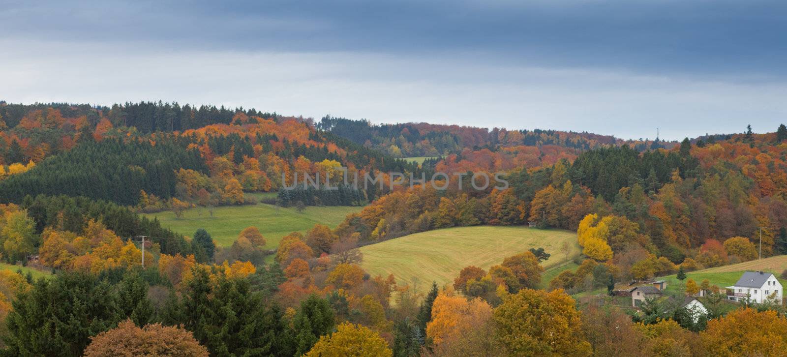 Valley with farmland, isolated house and forested hills in Eifel, rural Germany.