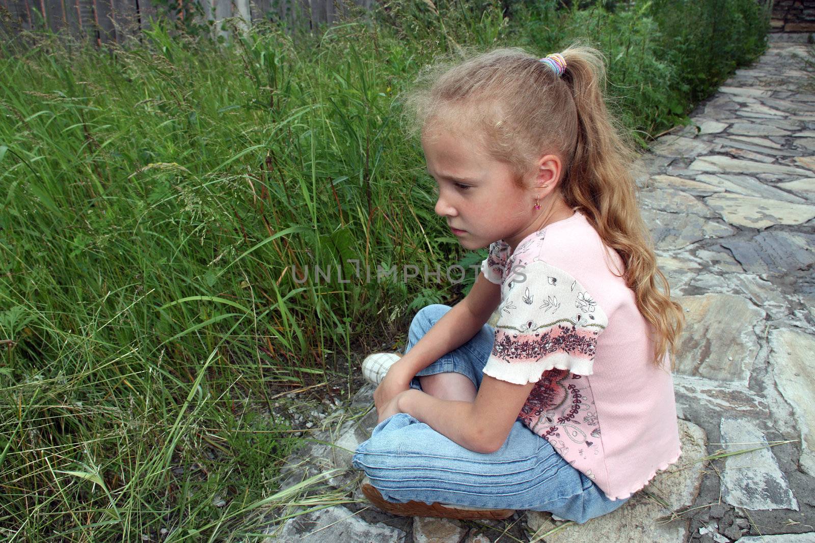sad little girl sitting in front of grass
