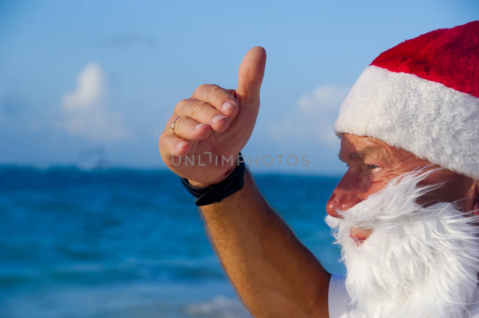 Santa claus is on vacation. He is looking at something on the beach.
