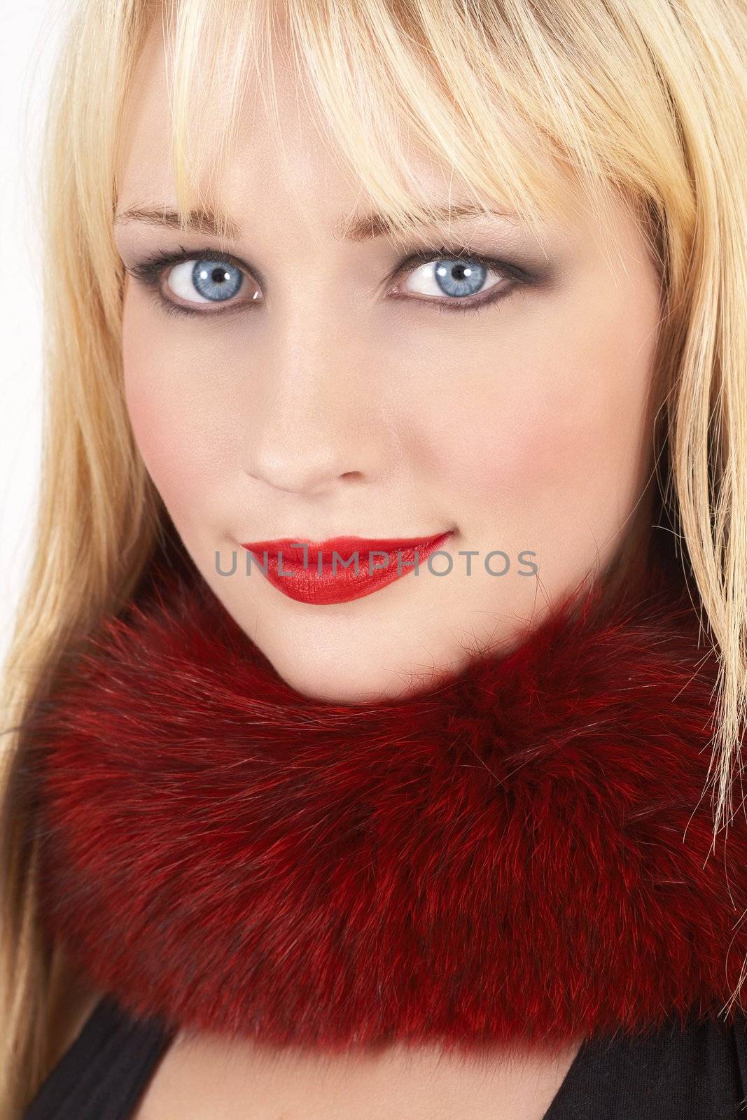 Portrait of a beautiful blonde woman with light blue eyes and bright make-up wearing red fur around her neck on white background