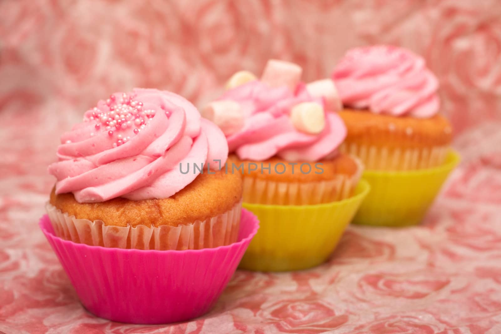 Three fresh vanilla cupcakes in pink and green cups with strawberry icing on decorative background