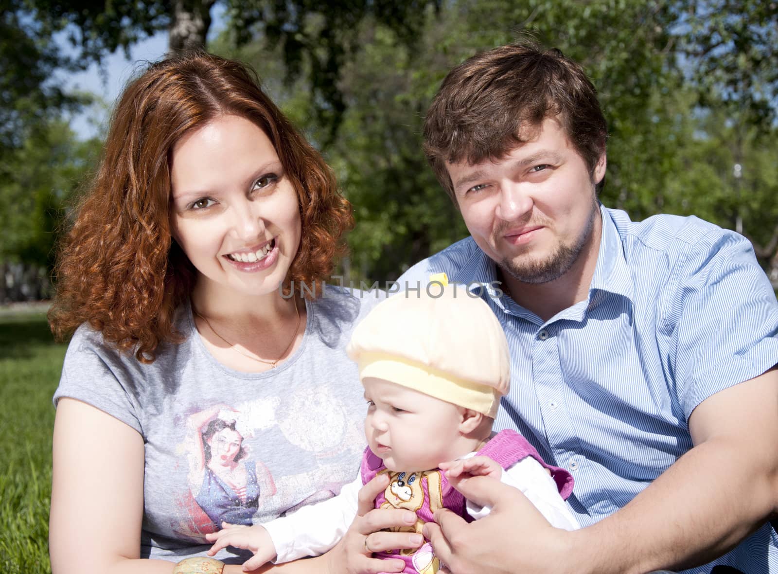 The young family in park, sits on a grass and smiles