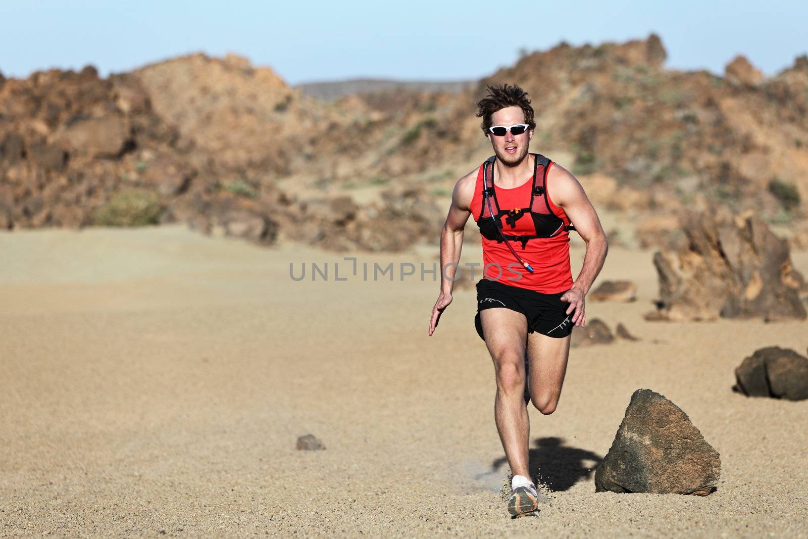 Male runner running / sprinting fast during adventure marathon run in beautiful desert landscape. Strong fit muscular fitness sport man model.