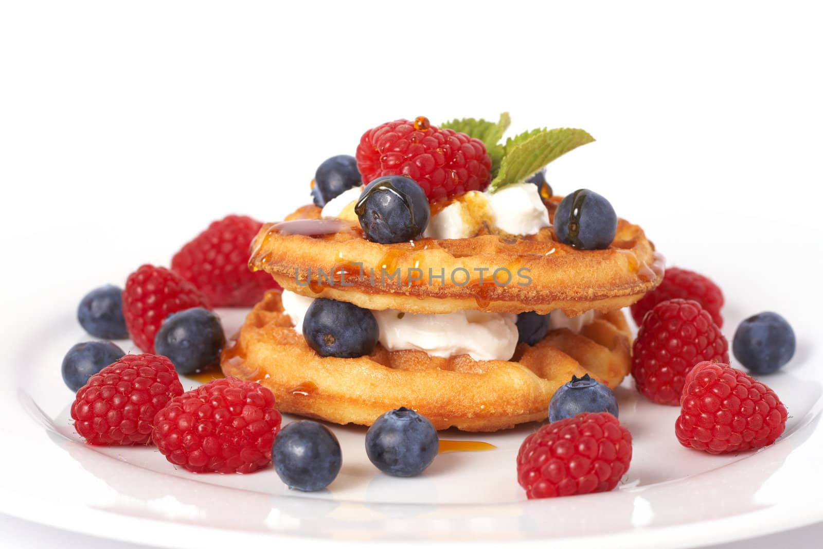 Belgian waffles with fresh raspberries, blueberries, mint leaves and cream on white plate