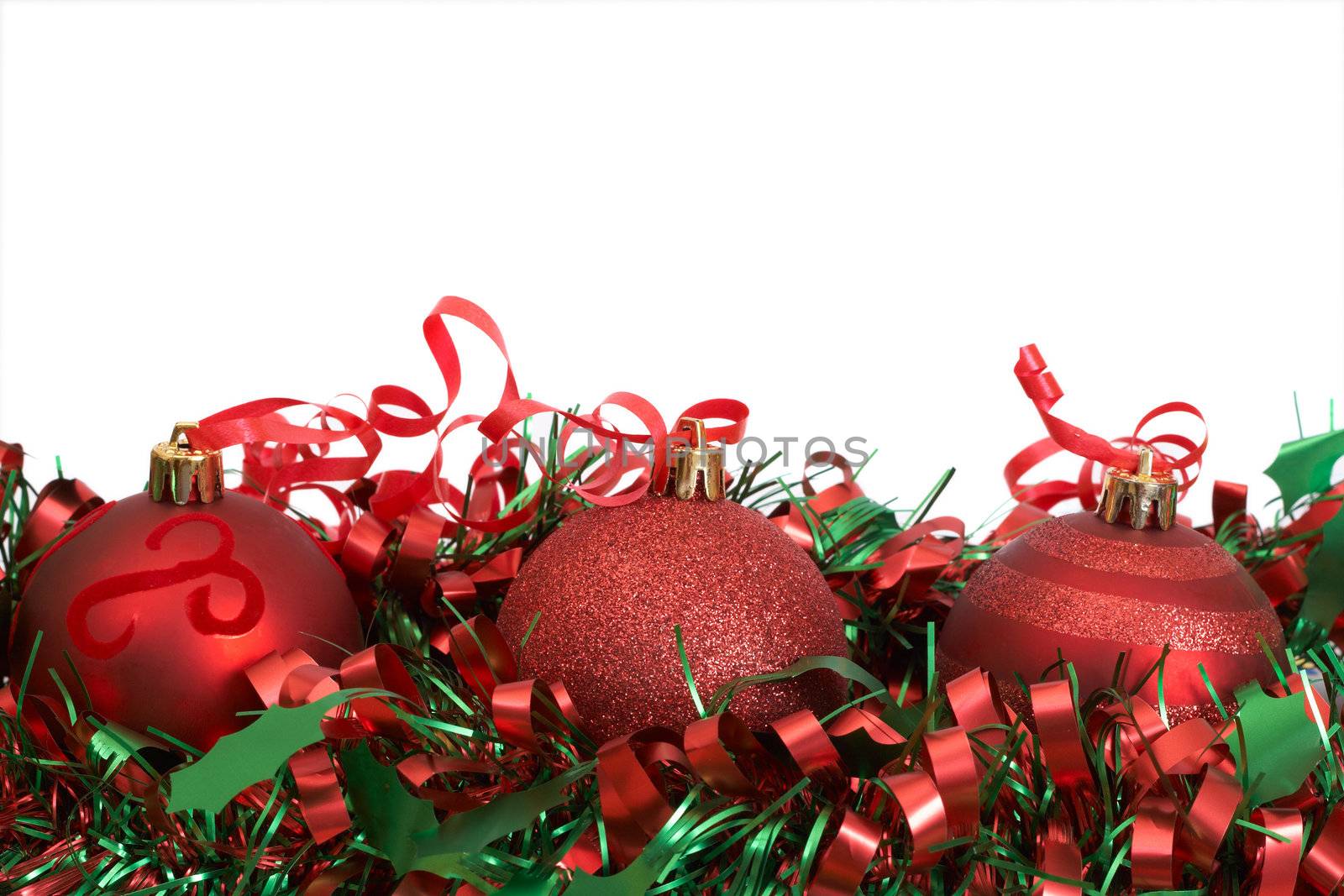 Three red Christmas baubles on green tinsel isolated on white background with copy space. 