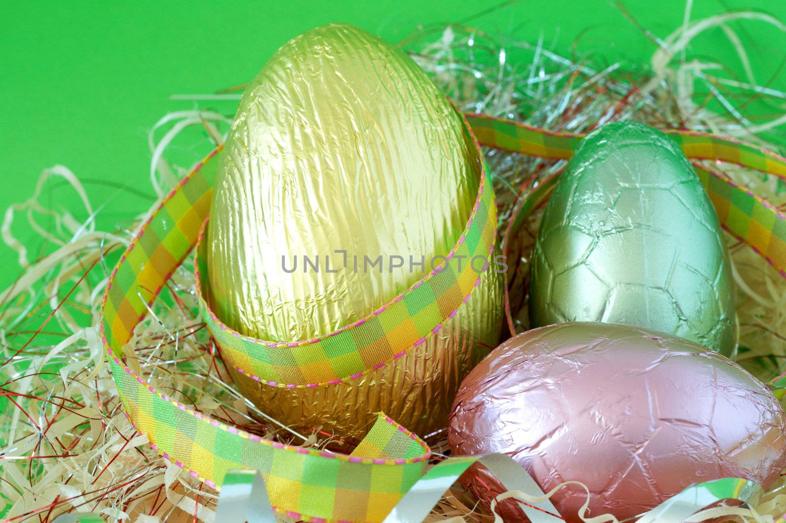 Assortment of chocolate Easter eggs wrapped in straw on green paper background