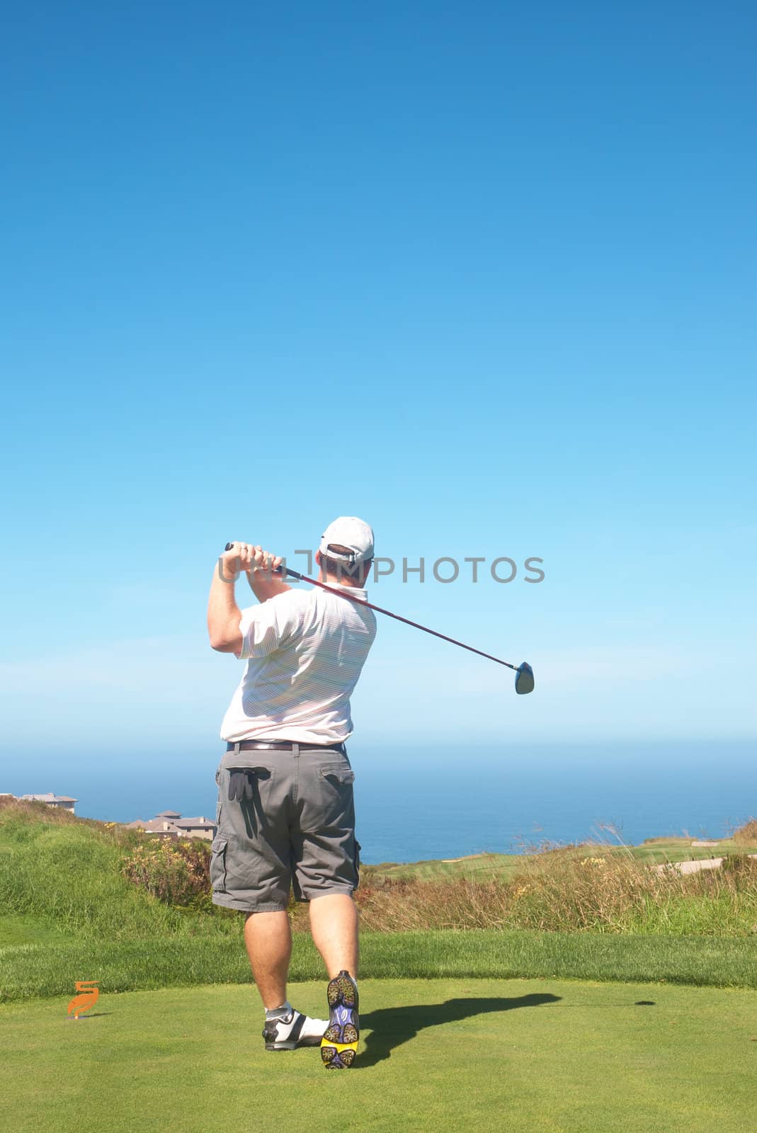 Young male golfer hitting the ball from the tee box next to the ocean on a beautiful summer day 