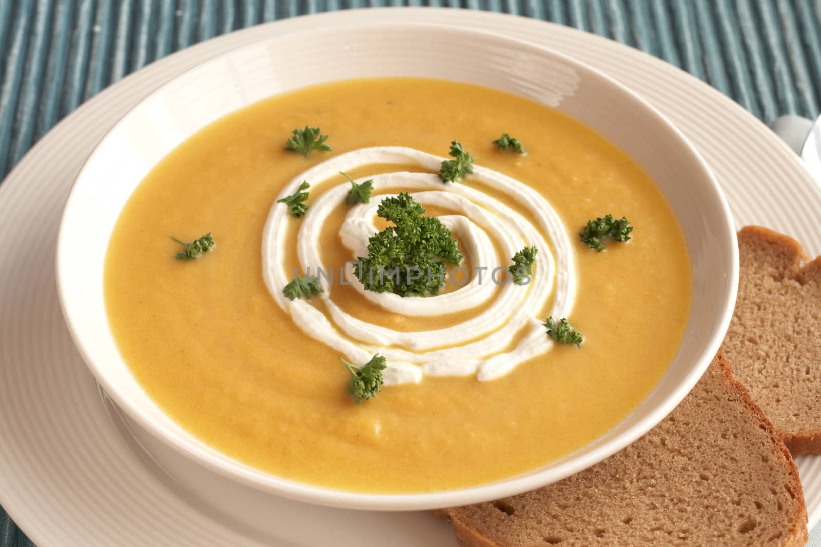 Bowl of fresh hot butternut soup with cream and parsley, served with rye berliner bread