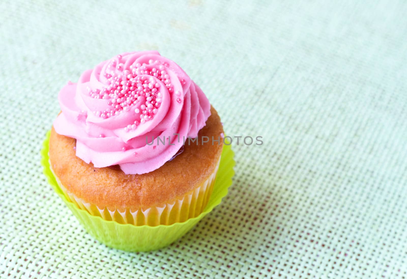 Fresh vanilla cupcake in green cup with strawberry icing on decorative background