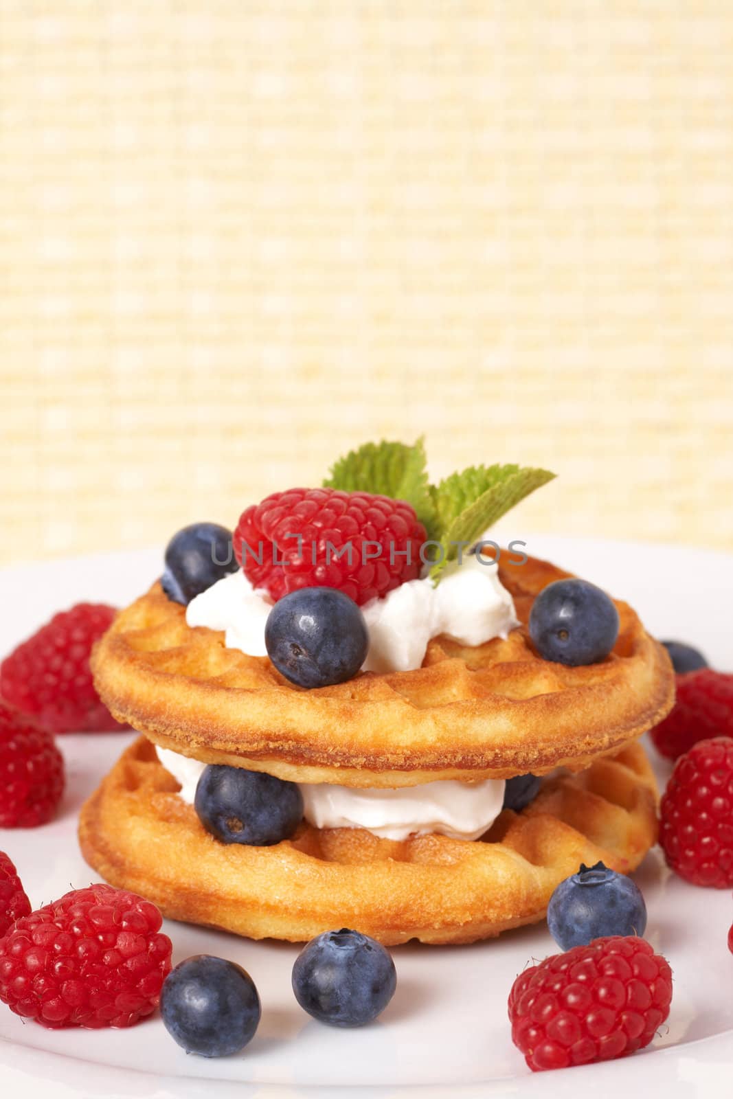 Belgian waffles with fresh raspberries, blueberries, mint leaves and cream on white plate