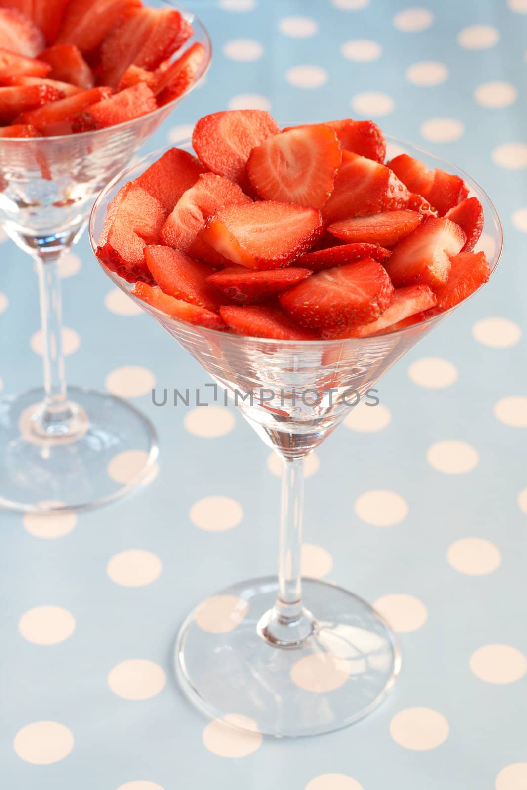 Sliced fresh strawberries in martini glasses on blue polka dot background