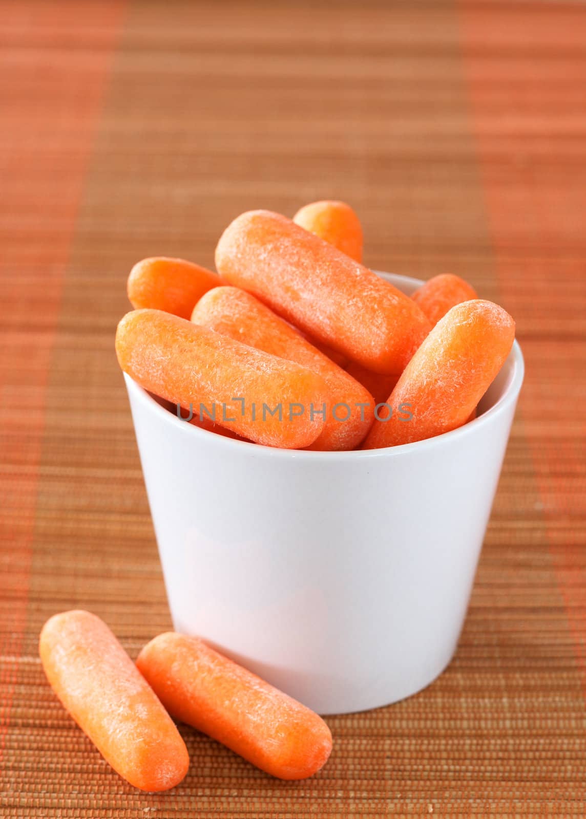 Fresh baby carrots in a small ceramic container on orange background