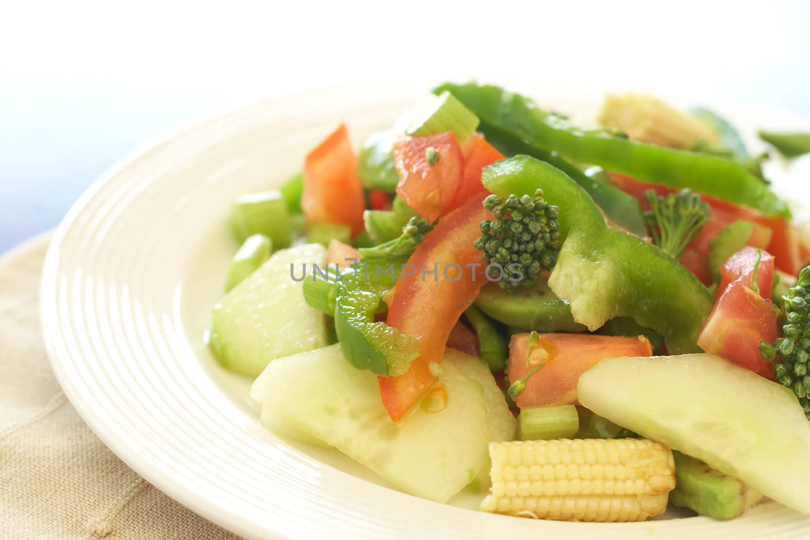 Fresh salad with cucumber, tomato, peppers, baby sweet corn and broccoli on white plate