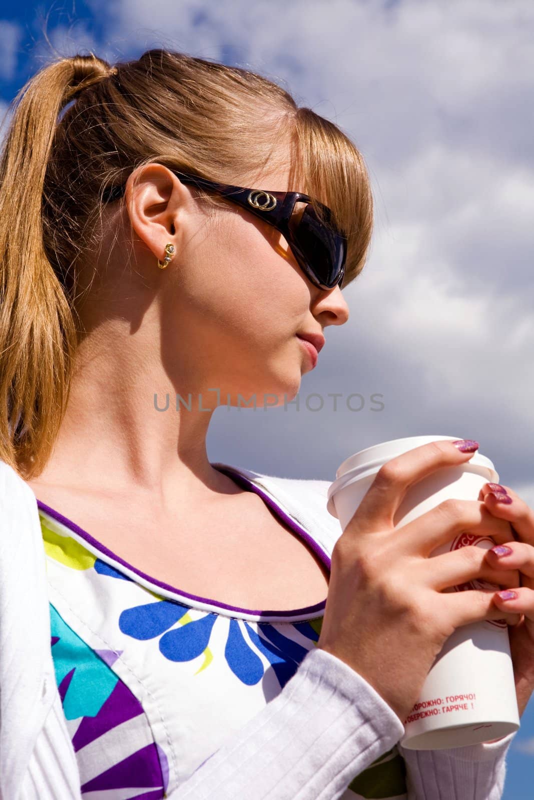 Blond lovely young woman drinking cup coffee outside