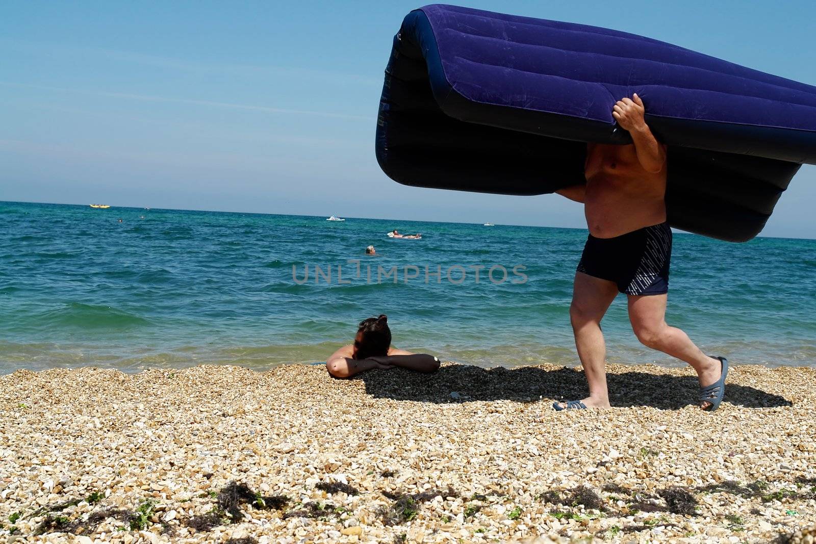 The person transfers a mattress to a beach