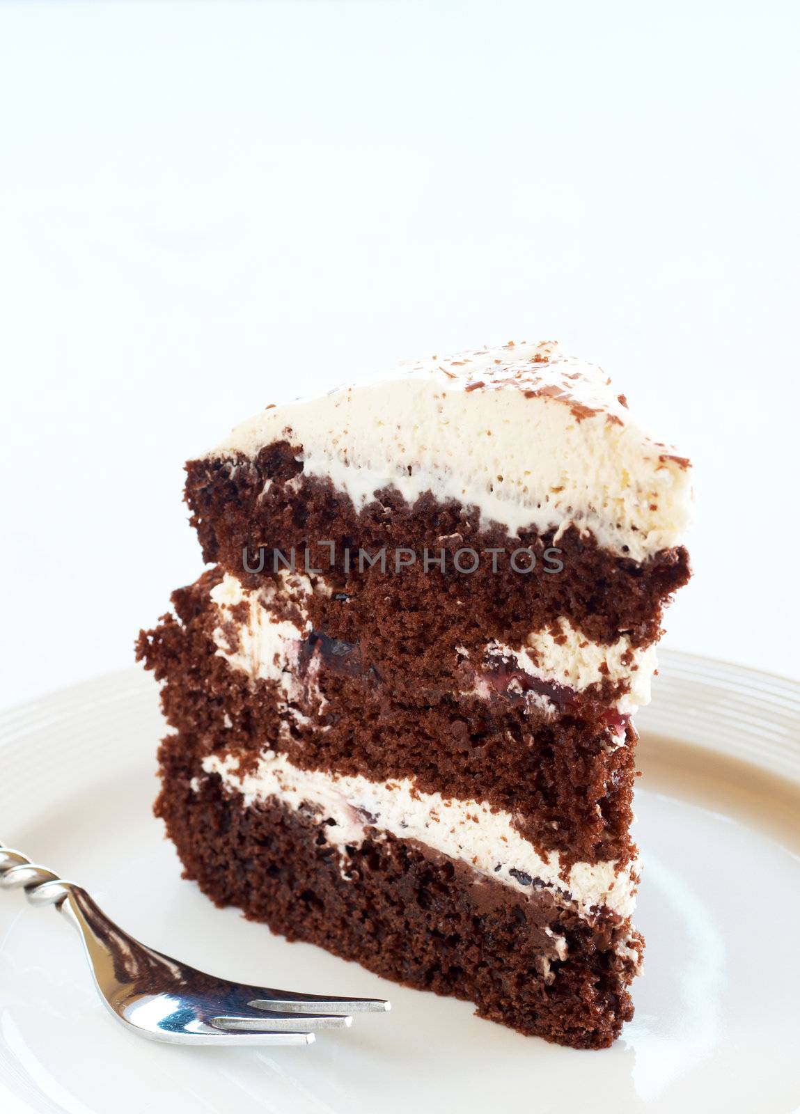 Slice of Black Forest cake with fresh cream and cherries, served on a white plate with silver fork