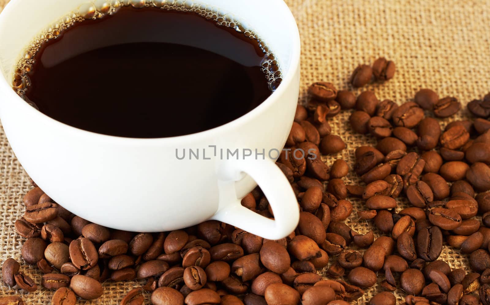 Cup of fresh brewed coffee with roasted coffee beans on straw placemat