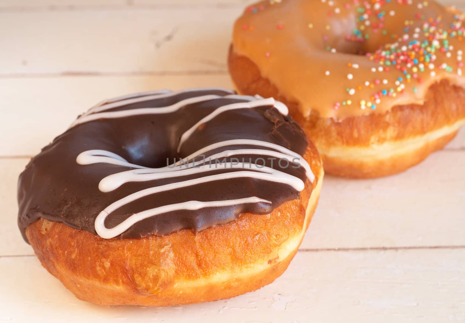 Two donuts covered in caramel and chocolate icing and sprinkles on grunge wooden background