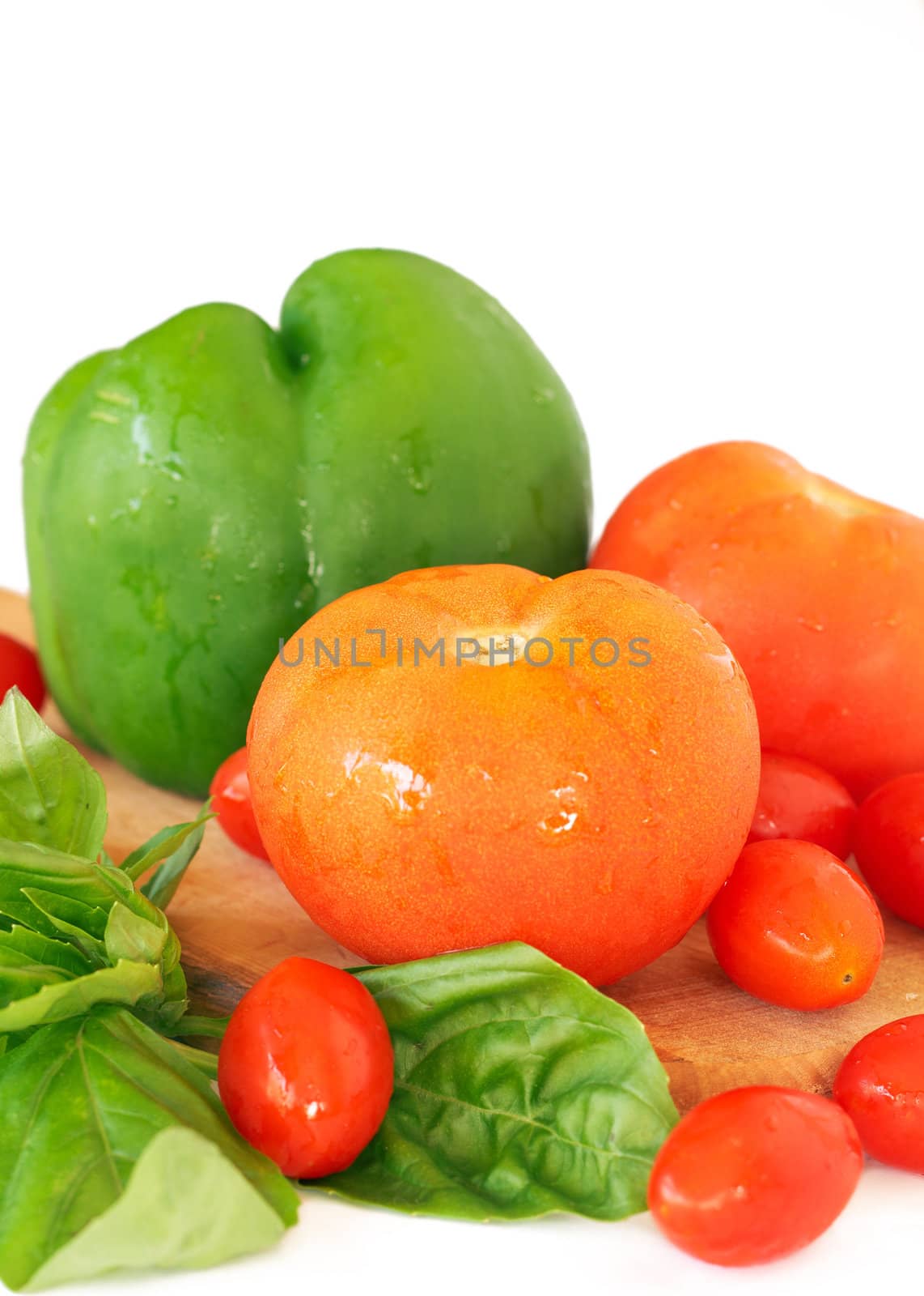 Fresh red tomatoes, green pepper and basil on wooden board isolated on white background