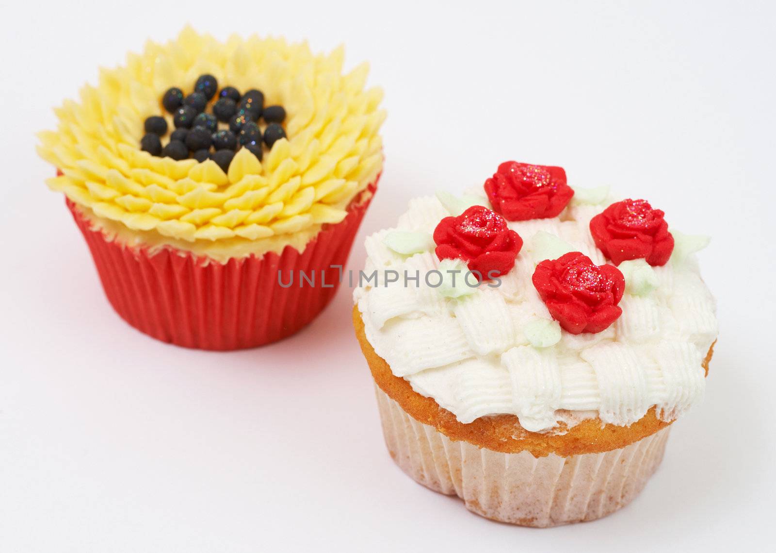 Two vanilla cupcakes with various decorations on white background
