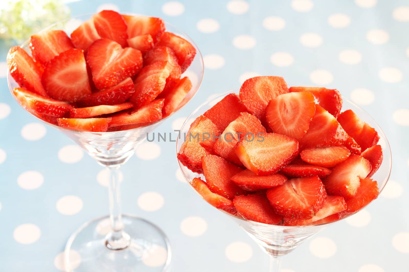 Sliced fresh strawberries in martini glasses on blue polka dot background