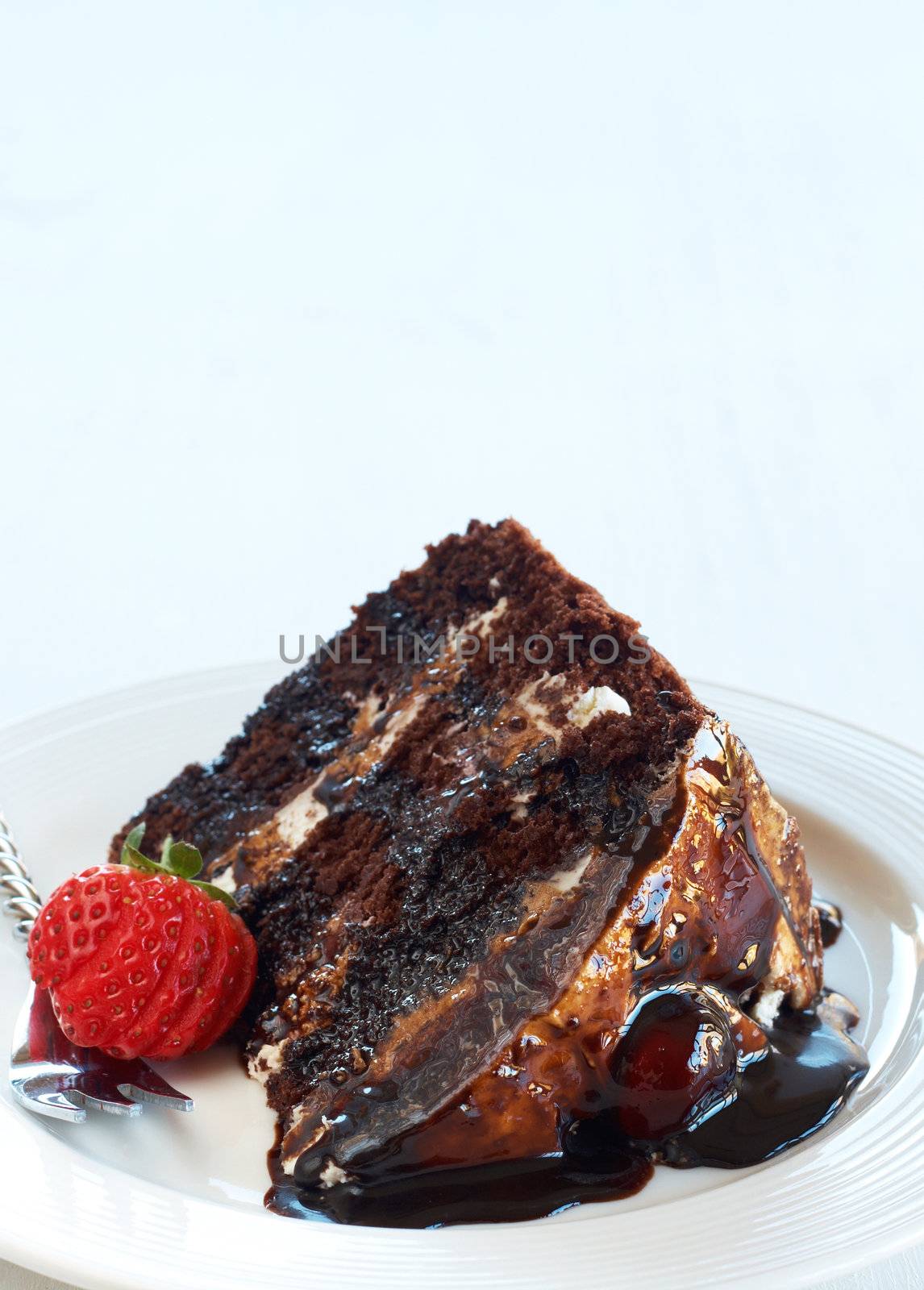 Slice of Black Forest cake with fresh cream and cherries, served on a white plate with silver fork and strawberry