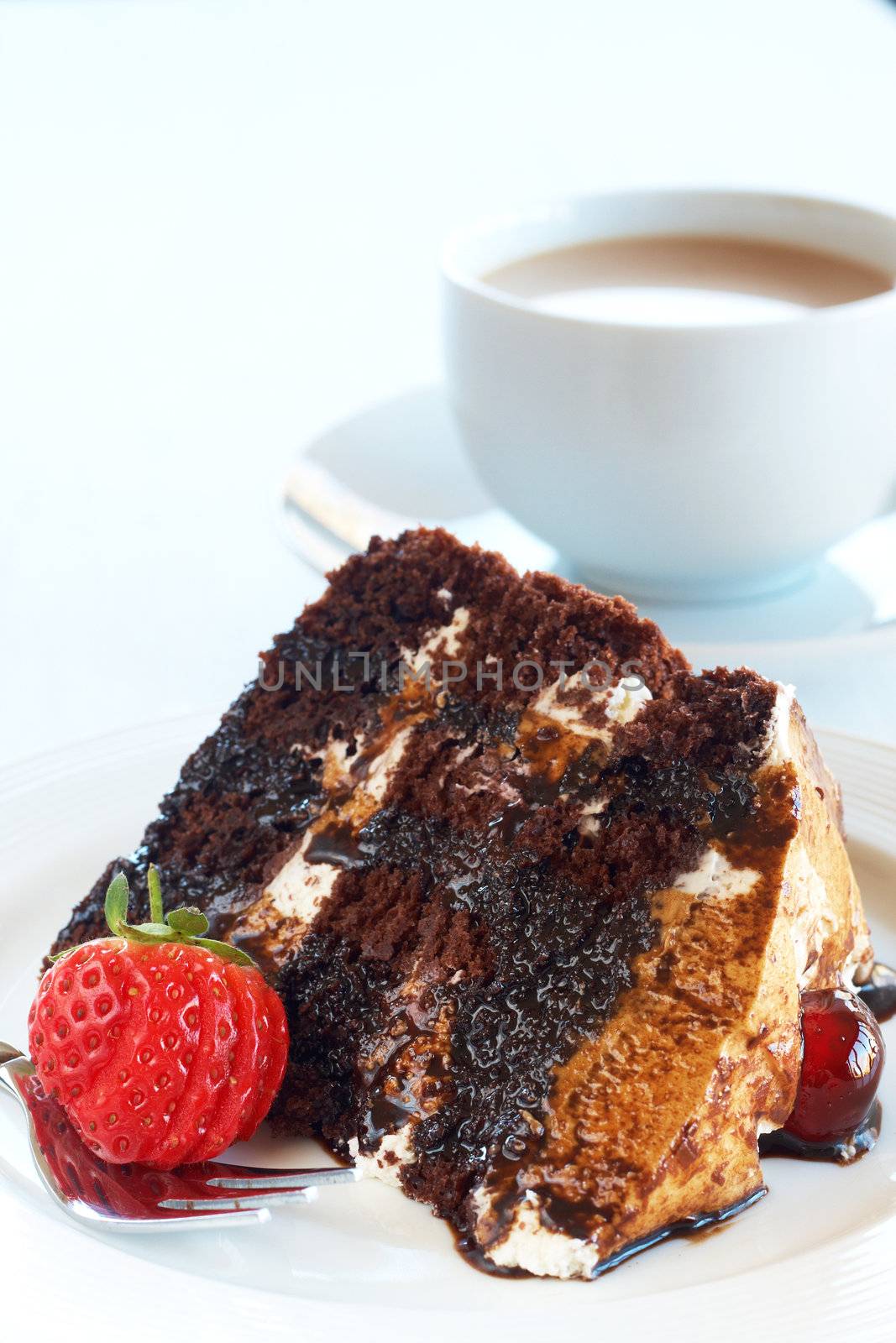 Slice of Black Forest cake with fresh cream and cherries, served on a white plate with silver fork and a cup of coffee