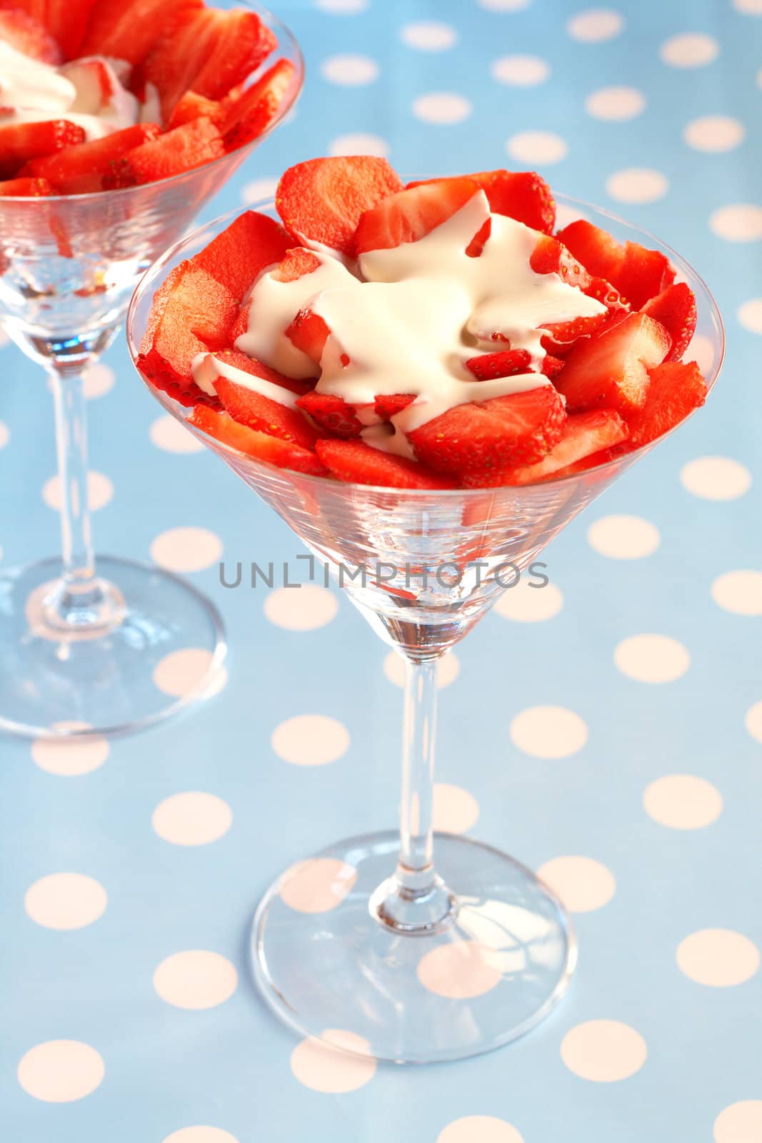 Sliced fresh strawberries with running cream in martini glasses on blue polka dot background