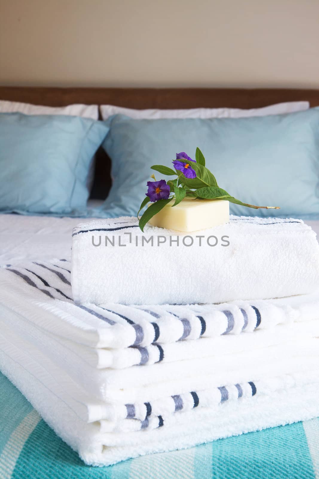 Beautiful bedroom interior with white sheets and striped towels with soap and flowers