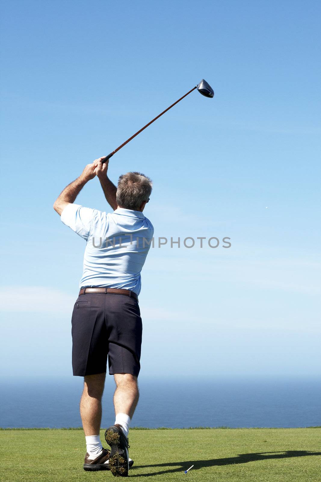 Senior male golfer playing off the tee box on a summer day