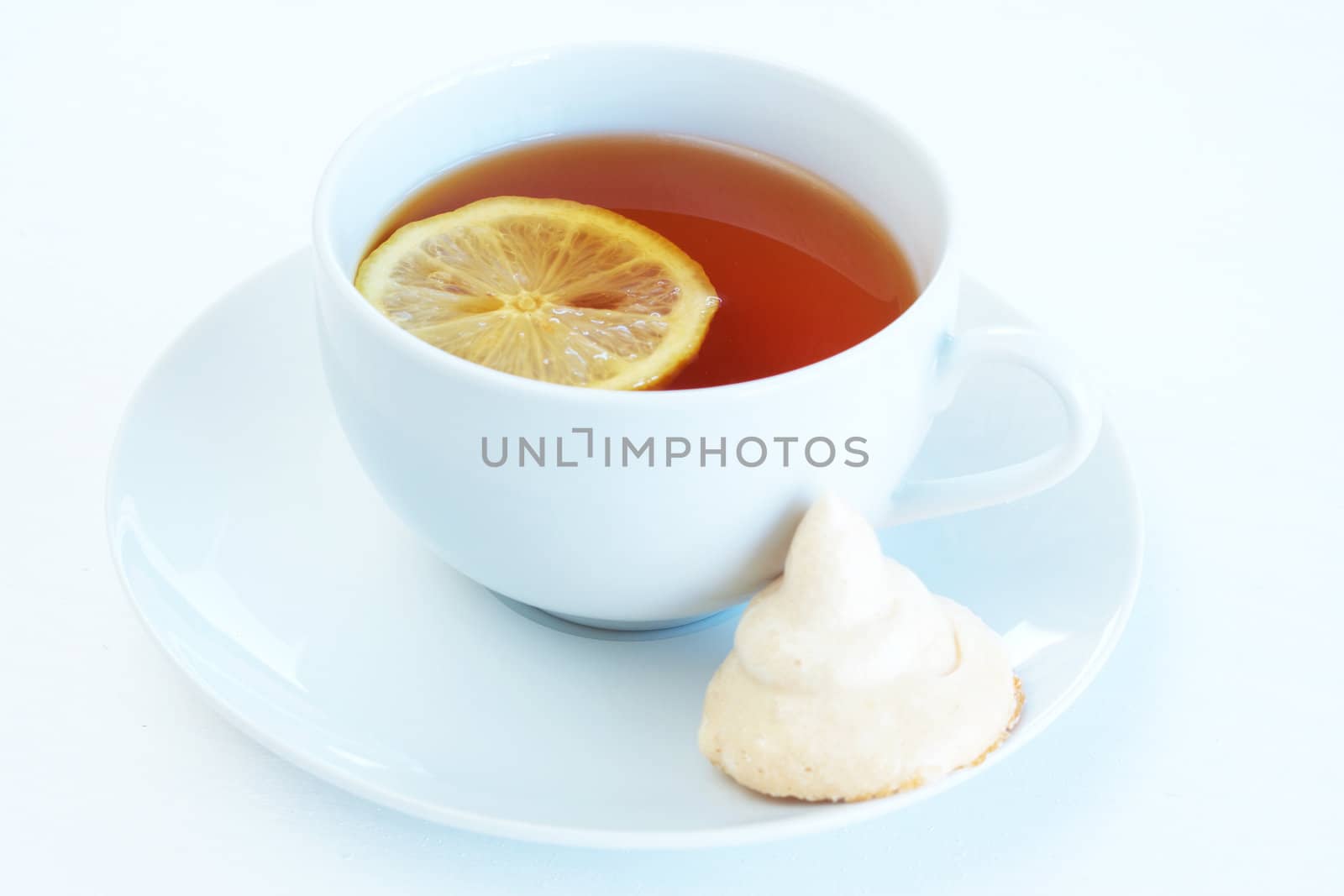 Cup of tea with lemon and meringue cookie on white background. Focus on the tea