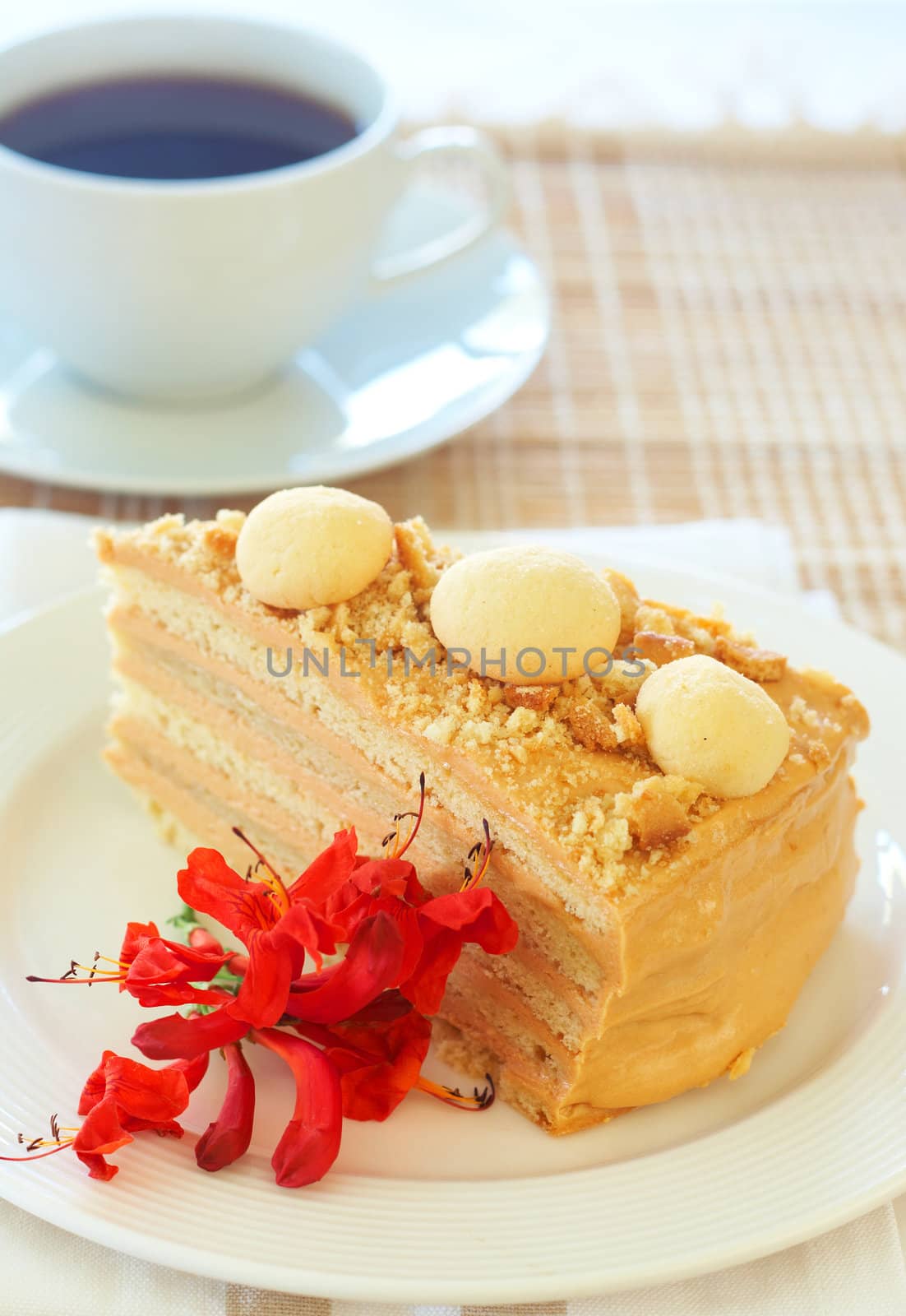 Slice of caramel Medovik cake made of honey and caramel cream, decorated with flowers with a cup of coffee