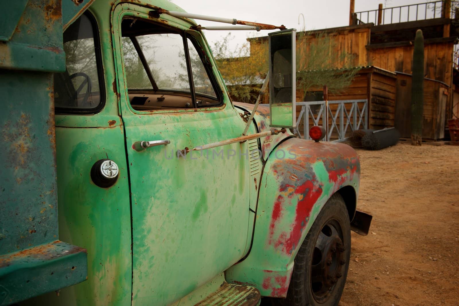 A Rusty old truck with patches of green and red paint in an old western town