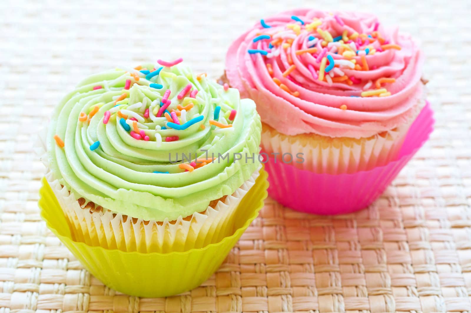 Fresh vanilla cupcakes with strawberry and lime icing on woven placemat background