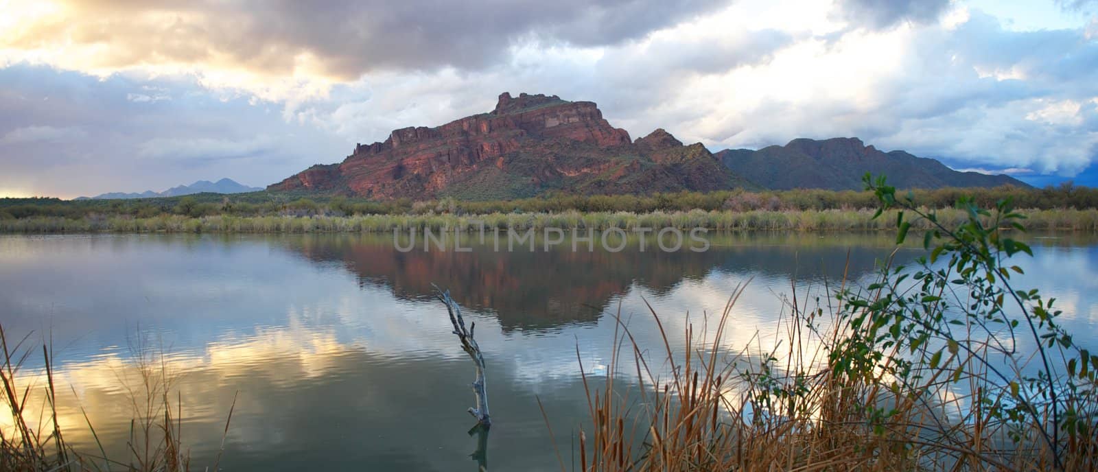 Beautiful green desert mountains with peaceful, calm river, plants, grasses, and large rain clouds