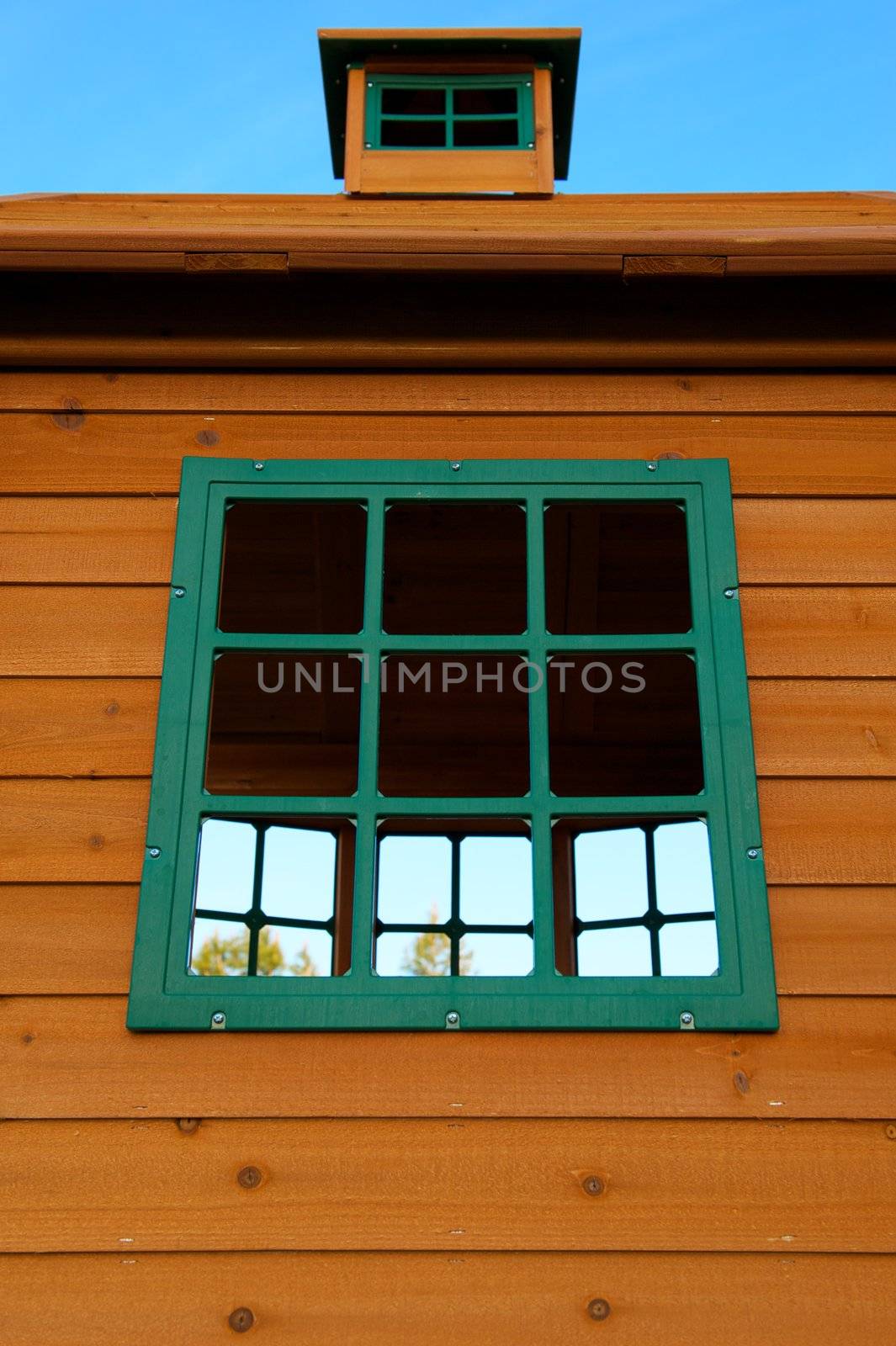 A Wooden House with knots and Green Plastic Windows that look out to trees and a blue sky