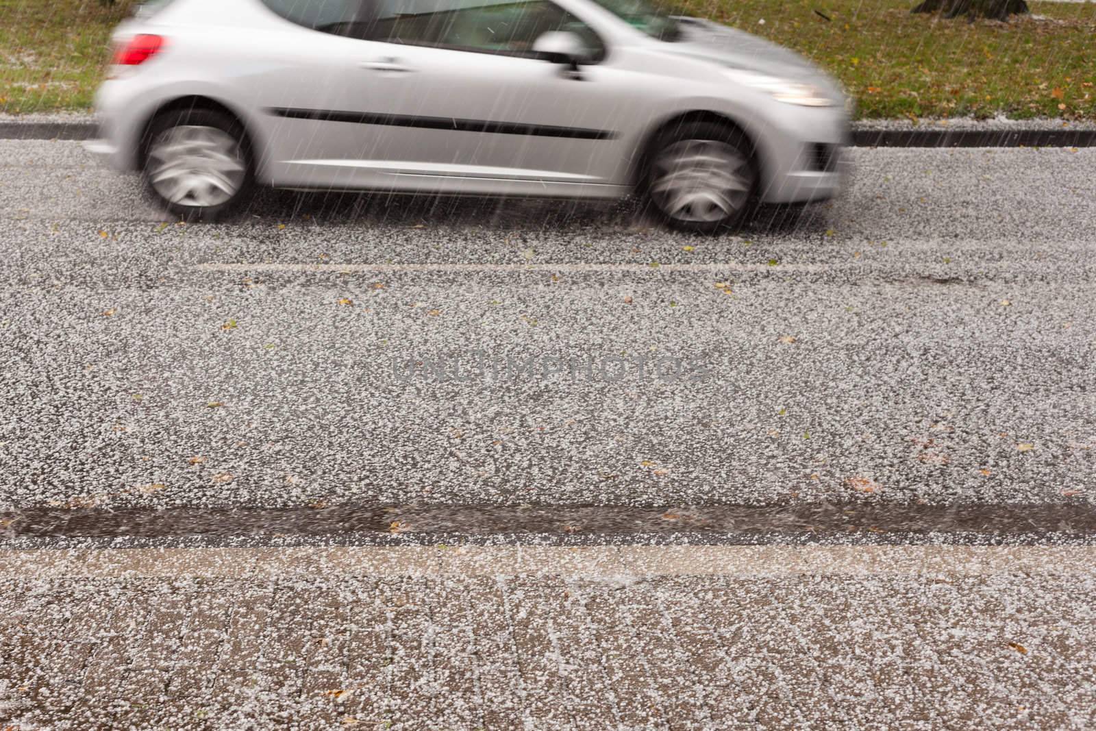 Small car driving on road through heavy hail storm.