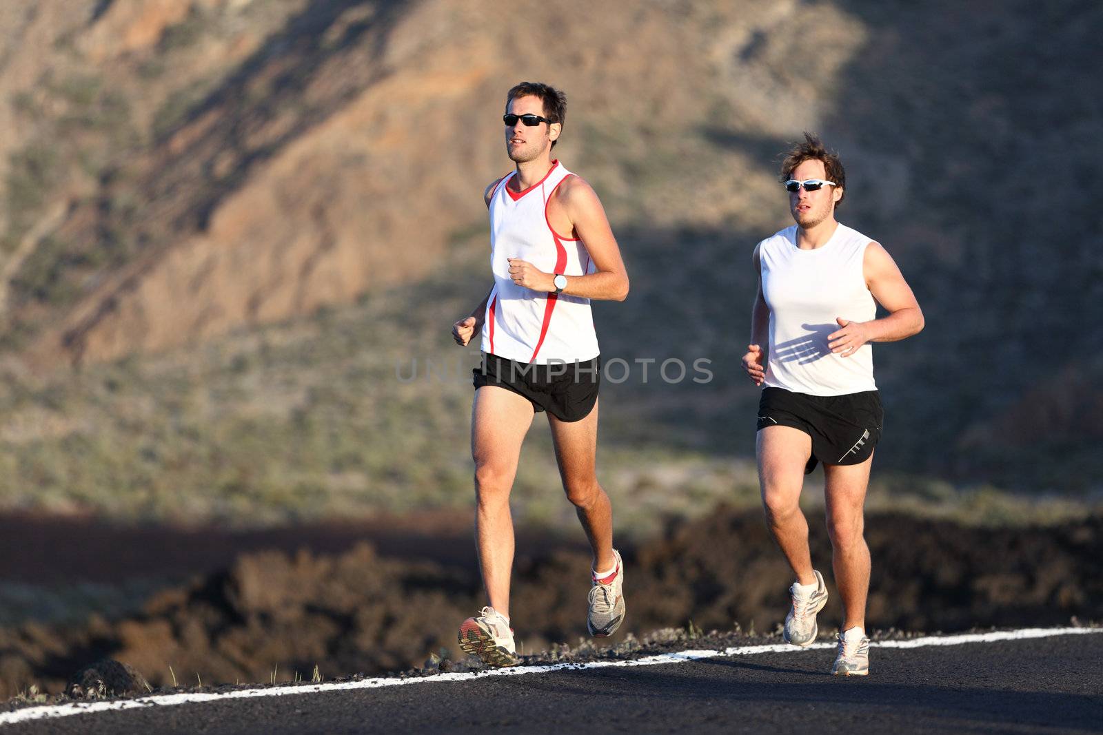 Runner men running marathon training run on road in amazing mountain landscape. Two men jogging in sporty outfit.