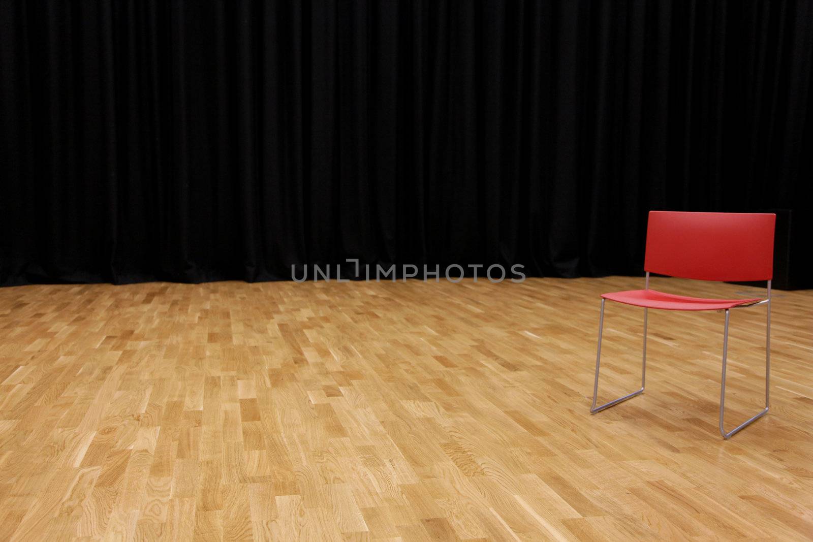 A directors chair on a stage with a blackcurtain in background by haiderazim