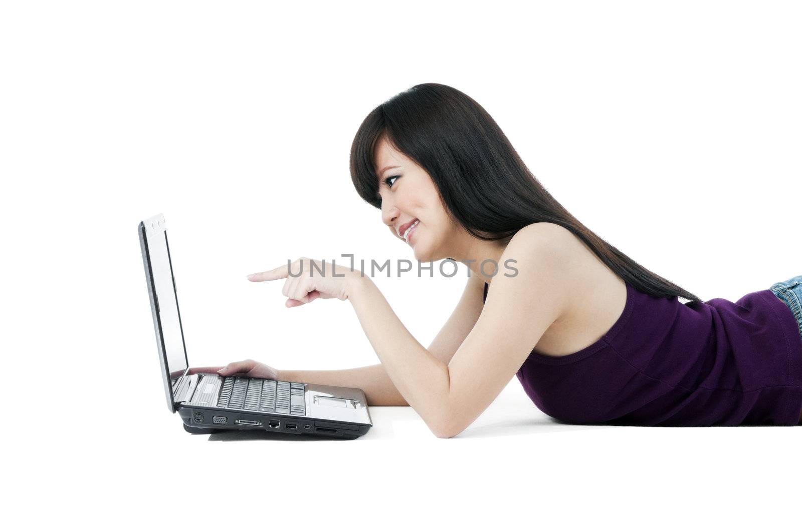Portrait of a young Asian woman lying on the floor and pointing at laptop over white background.