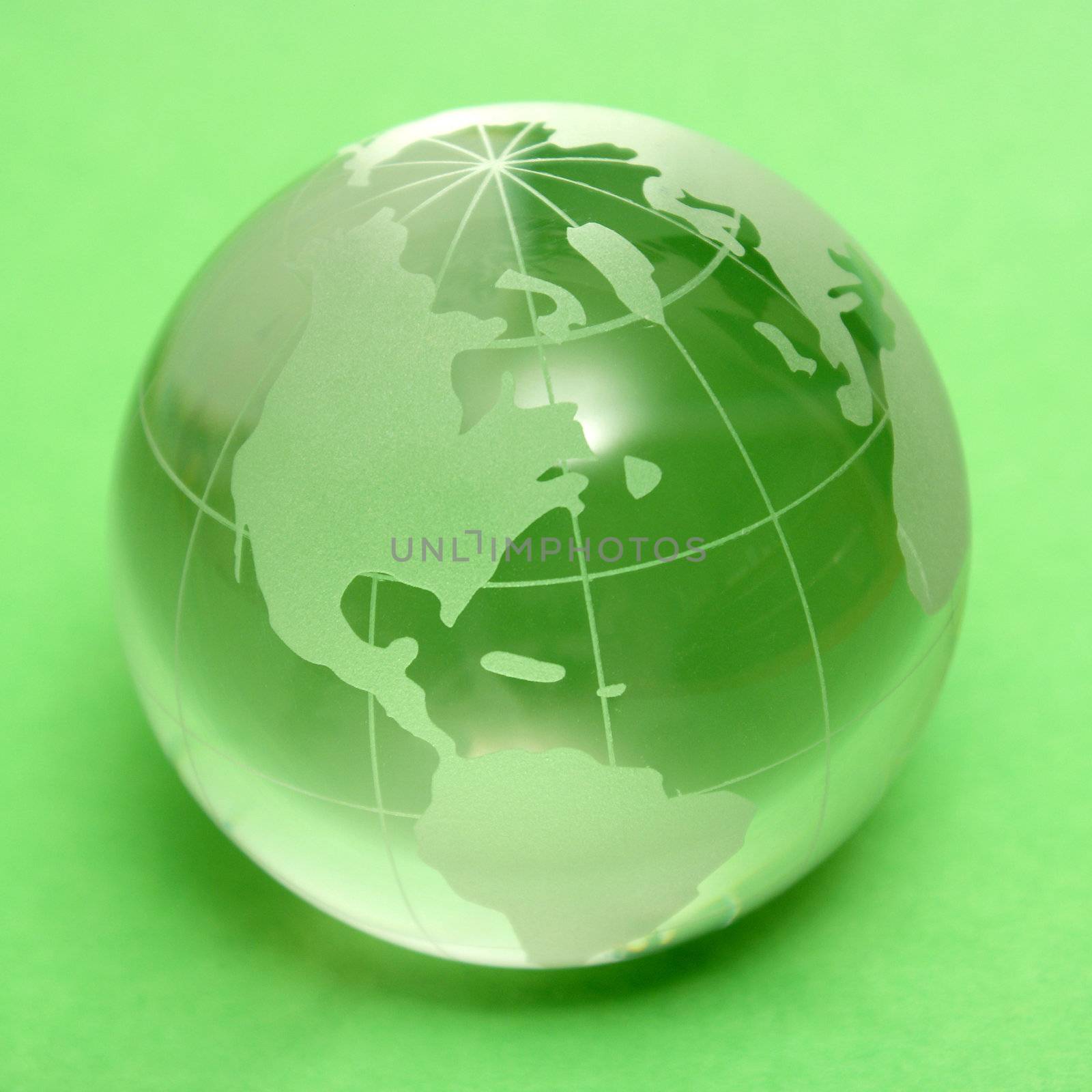 A square format shot of a glass globe of earth over a green background.
