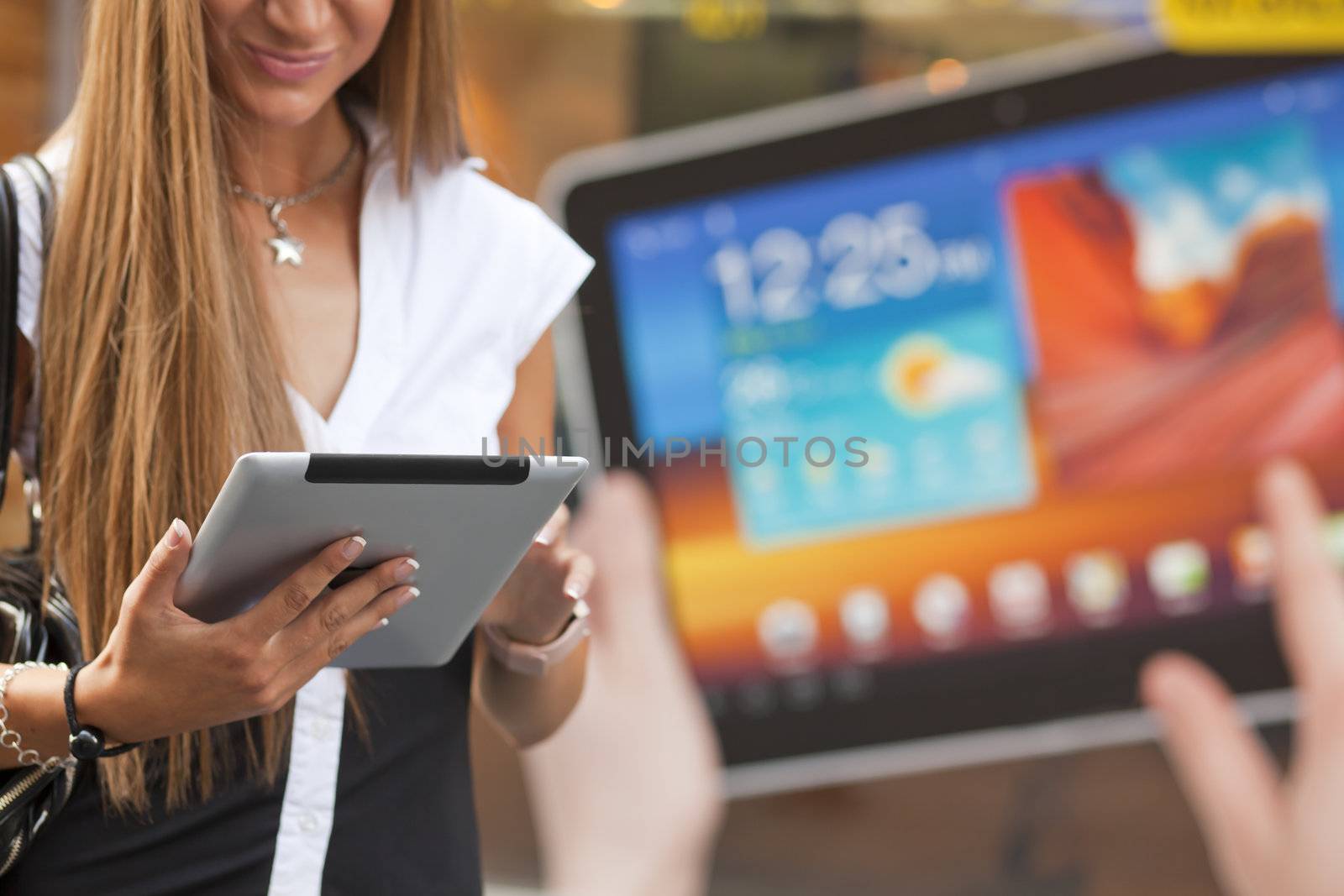 Young Woman with tablet computer walking on street, downtown. In background is blured advertisiment with OpenSource graphics. Visible noise