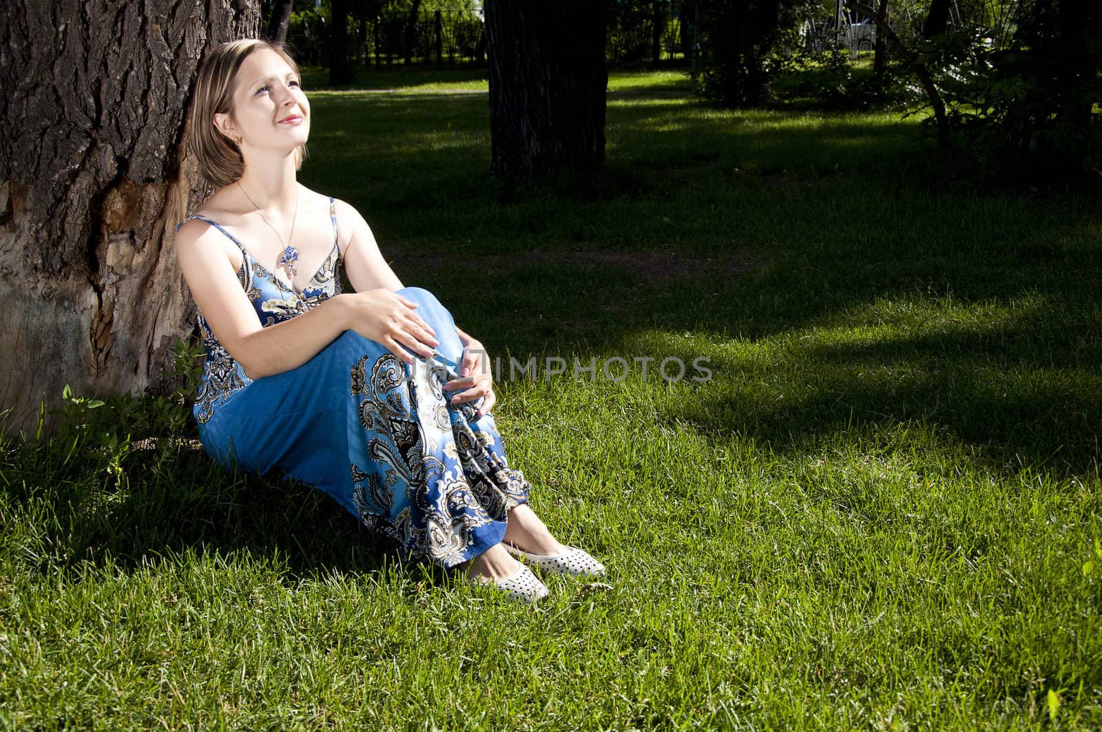 beautiful woman sitting under a tree in park and smiling