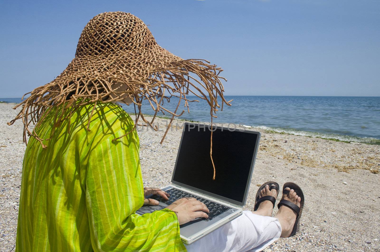 Woman sitting on beach in green top working on laptop
