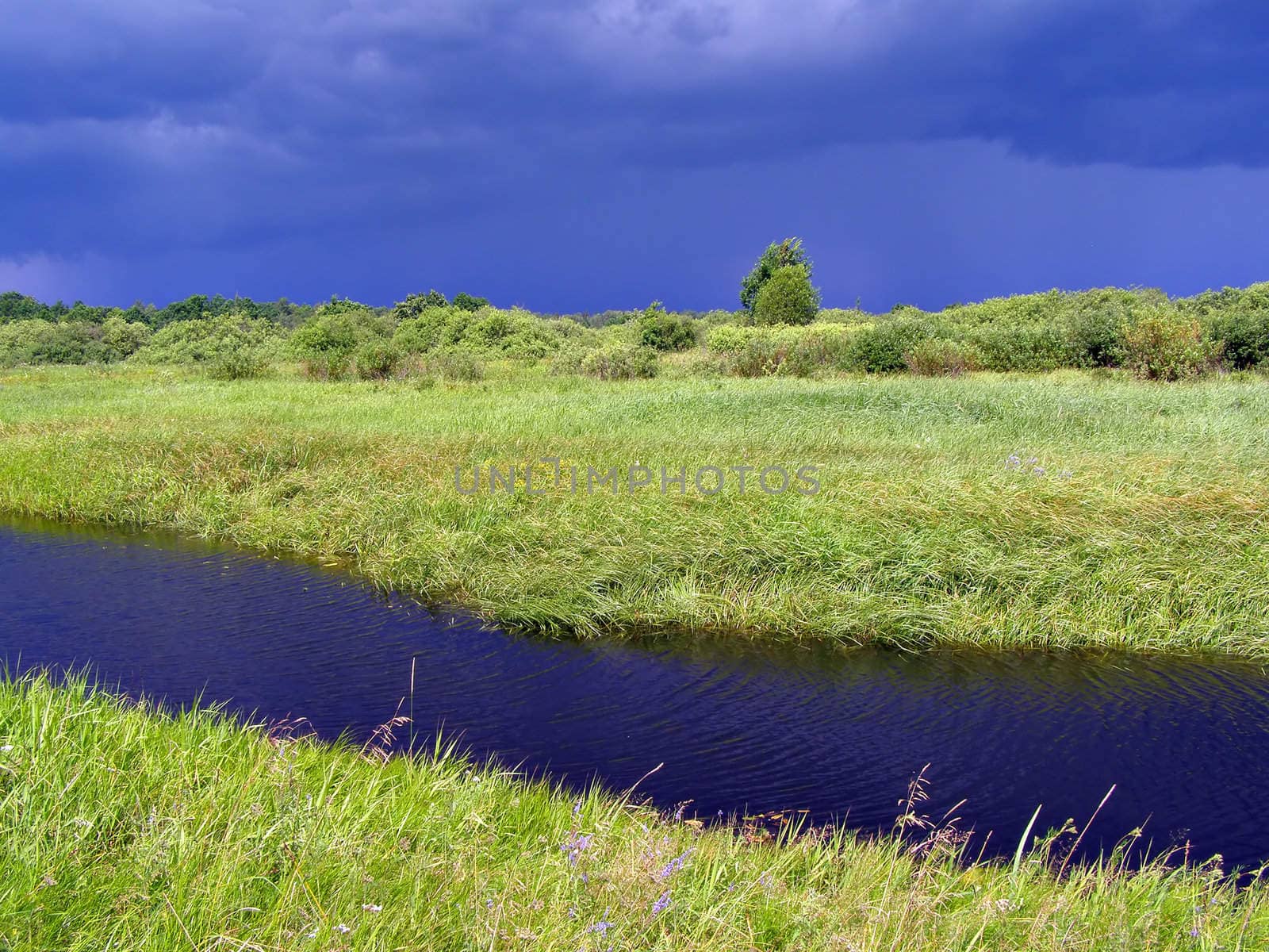small river on green field before thunderstorm